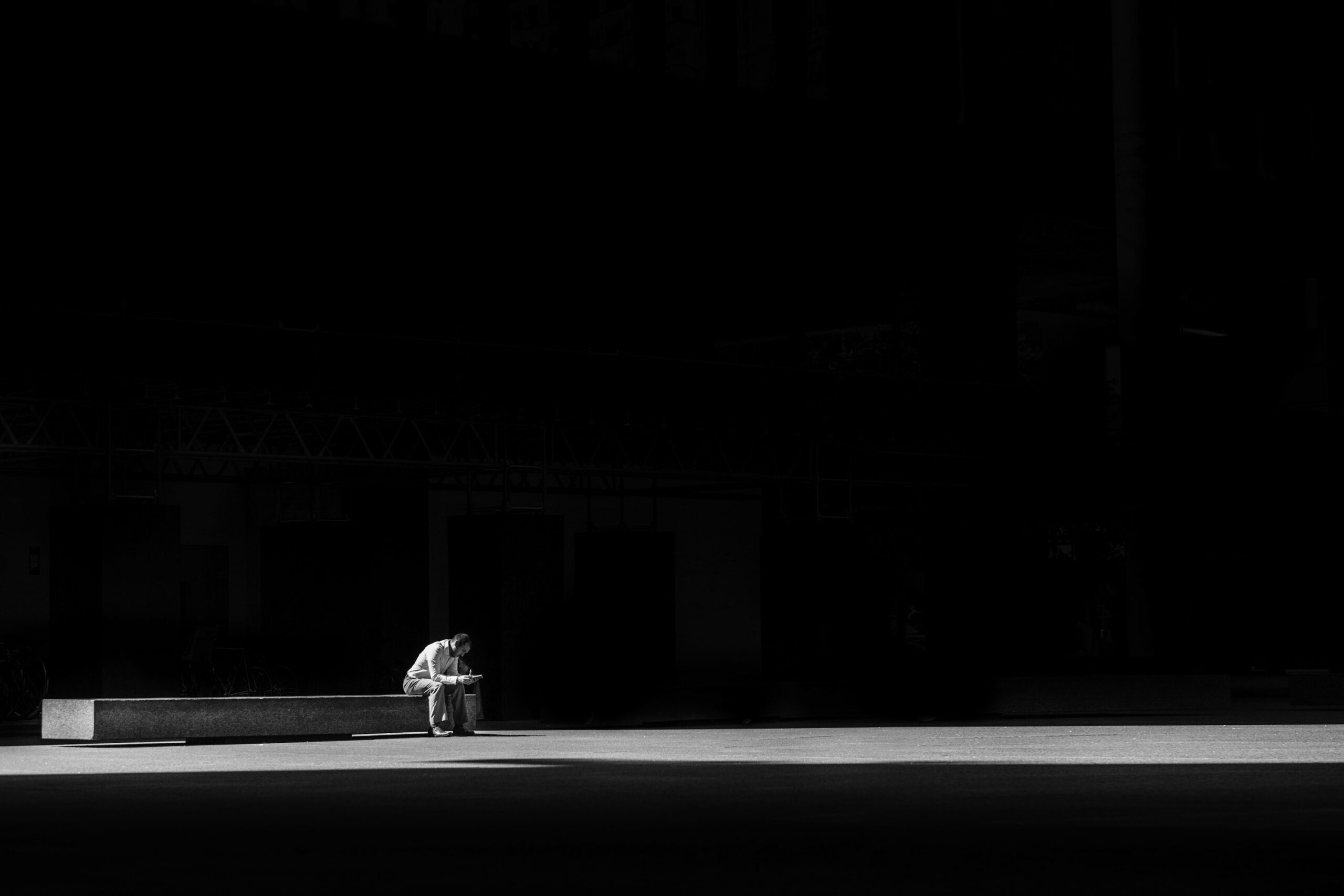 Photogaphie en niveaux de gris d’un homme assis sur un banc en béton
